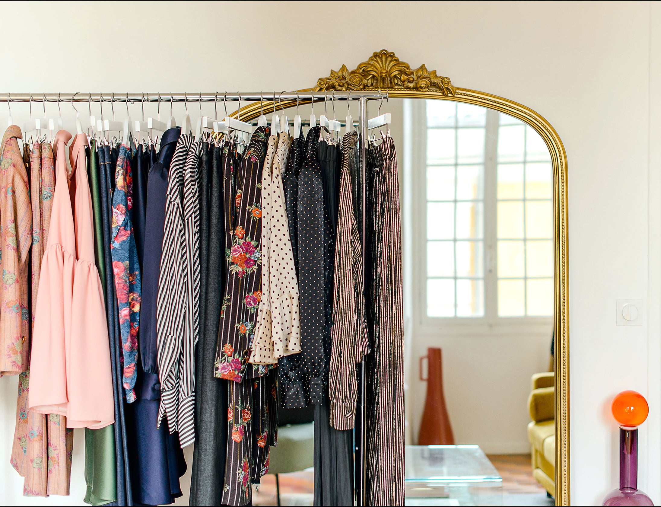 Beaux vêtements suspendus sur un portemanteau devant un miroir doré vintage